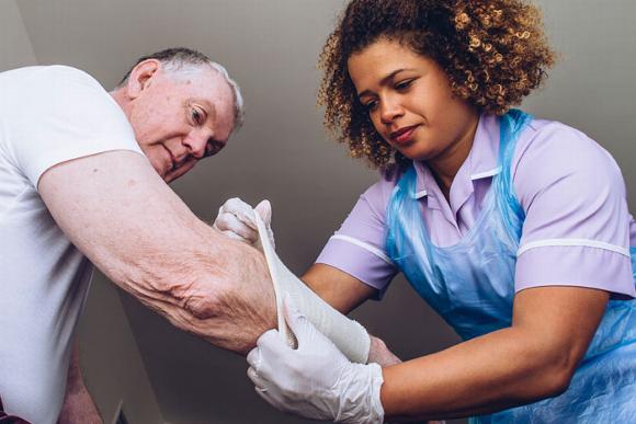 carer helping elderly man put dressing bandage on arm