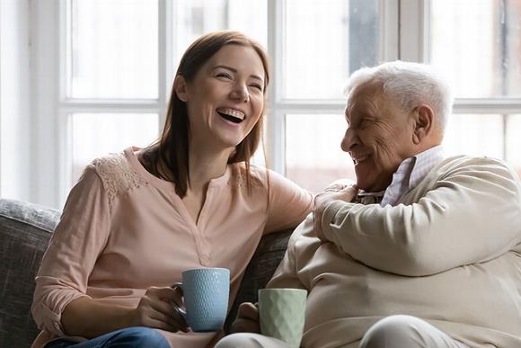 lady sitting on couch with older man laughing and drinking tea
